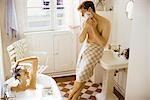 Couple together in bathroom, woman bathing, man leaning against sink, shaving