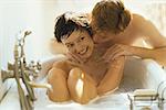 Woman relaxing in bathtub, husband kissing her cheek