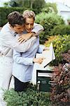 Couple checking mail together, man embracing woman from behind