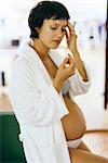 Pregnant woman holding head, looking at pill in hand