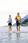 Young couple running together through shallow  water near shore