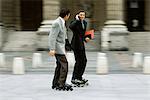 Männer im Geschäft Kleidung Inlineskating zusammen auf Bürgersteig, einer telefonieren