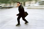Mann im Geschäft Kleidung Inline skating tragenden Aktenkoffer in Stadt-Quadrat
