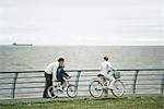 Father helping son learn to ride bicycle, mother watching