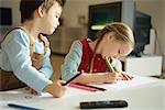 Siblings drawing with colored pencils, little boy pausing to look over sister's shoulder