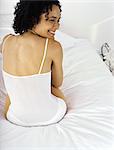 Young woman sitting on bed in underwear, looking away smiling