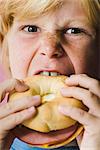 Boy biting into ham and cheese bagel sandwich, close-up