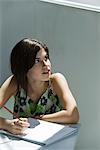 Teenage girl with pen and notebook, looking over shoulder out window