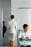 Female executive walking through office while colleagues work, rear view