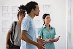 Male college student staring with disbelief at results posted on bulletin board, friends watching in background