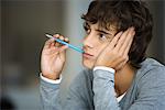 Young man daydreaming, absently holding pen in mouth