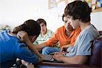 Young man using laptop, friends sitting on either side looking at display