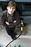 Man standing with arms folded refueling vehicle at gas station