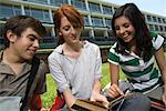 Hight school student showing friends passage in book, sitting together on school lawn