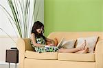 Teenage girl relaxing on sofa using laptop in living room