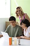 Mother observing teenage son and daughter using laptop computer