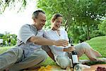 Couple d'âge mûr ayant pique-nique en plein air, ouvrir la bouteille de vin