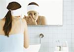 Femme debout devant le miroir de salle de bains, insertion de lentilles de contact
