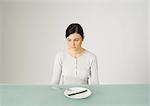 Young woman sitting in front of plate with single asparagus, looking away