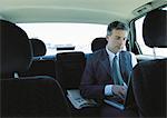 Businessman using laptop in backseat of car