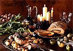 Dishes of meats, fruits and vegetables, with carafe of wine and candles in background