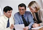 Two businessmen and a businesswoman examining document