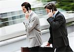 Two businessmen holding briefcase and cell phone, walking outside