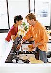 Couple smiling face to face over counter, man washing dishes, woman drying bowl