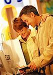 Man and woman with shopping bags, paying for purchase with check, waist up