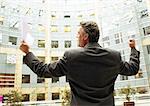 Homme debout devant le bâtiment, les bras levés en geste victorieux, vue arrière