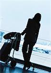 Businesswoman standing next to luggage in airport, silhouette.
