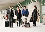 Group of business people walking with luggage outside airport terminal