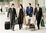 Group of business people walking in front of terminal with luggage.