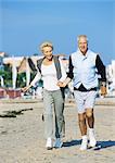Mature couple holding hands walking on beach, front view, full length