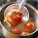 Close-up of cooked tomato held on skimmer over pot
