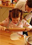 Girl using rolling pin, woman looking over girl's shoulder
