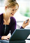 Woman using laptop computer and holding credit card, laughing