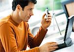 Man holding cell phone, looking at laptop computer