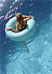 Young girl floating in pool in inner tube, shot from above.