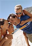 Close-up of two men carrying women on their backs on the beach.