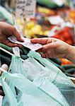 Hands exchanging money over plastic grocery bags, blurred stalls in background