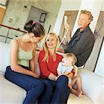 Mature man, woman, teenager and baby sitting on sofa