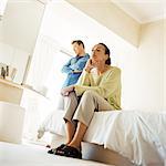 Man standing with arms crossed, behind woman sitting on edge of bed, low angle view