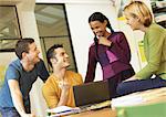 Four people smiling around desk with laptop computer