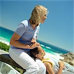 Girl with head on mother's lap, sea in background