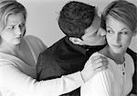 Man standing between two women, kissing one of them, b&w