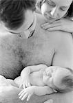 Father holding sleeping infant, mother looking over father's shoulder, b&w