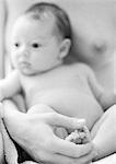 Infant leaning against mother's chest, mother holding infant's feet in hand, close-up, b&w