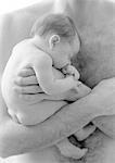Father holding sleeping infant against bare chest, b&w