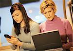 Two young women, one using laptop, one using phone